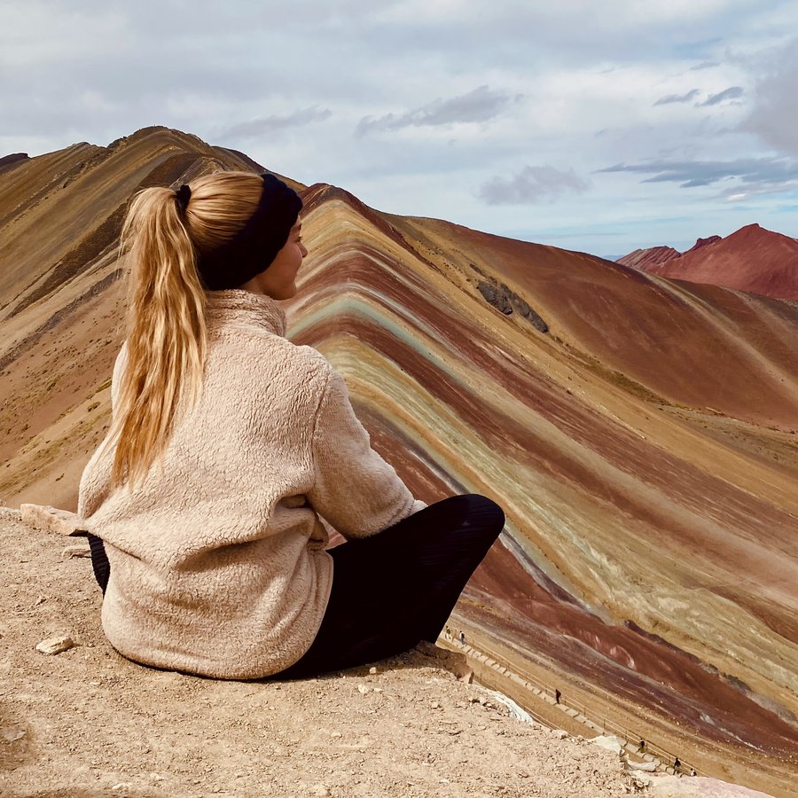 Catharina sitzt vor den farbig gestreiften Bergen des Rainbow Mountain